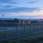 Editorial illustration of a prison perimeter fence at dawn. Not the actual facility.